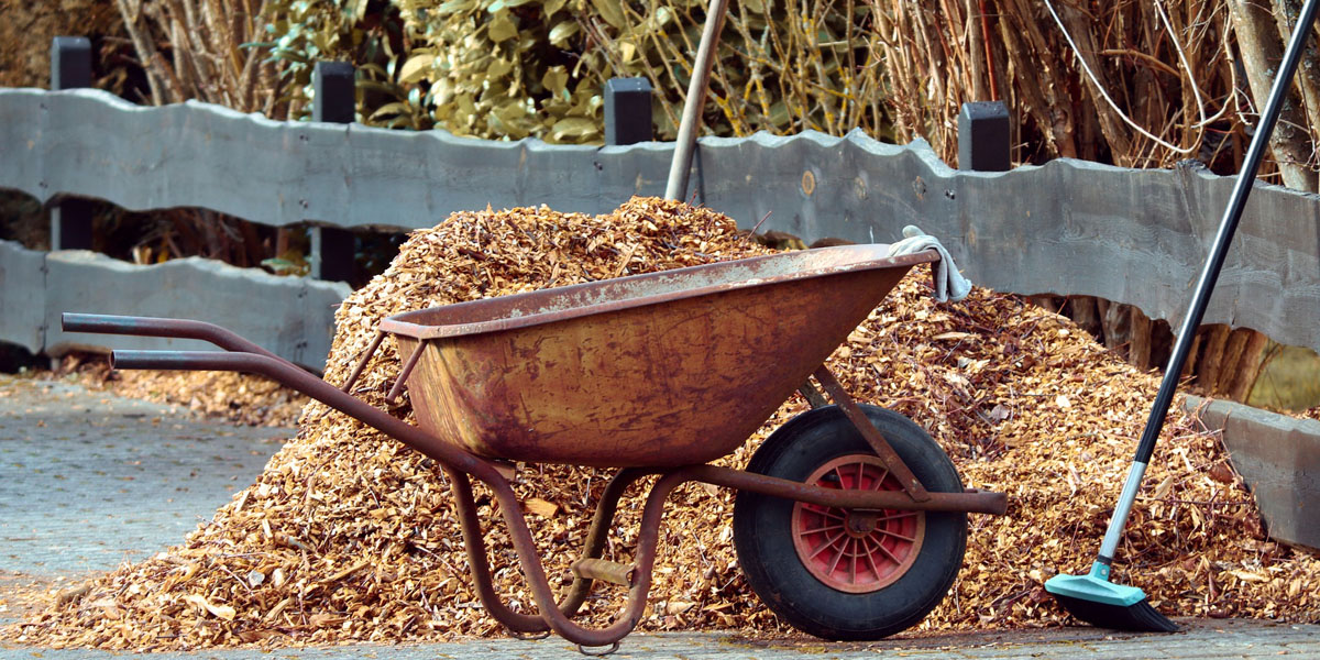 Wood mulch piled up on a driveway with a wheelbarrow in the foreground